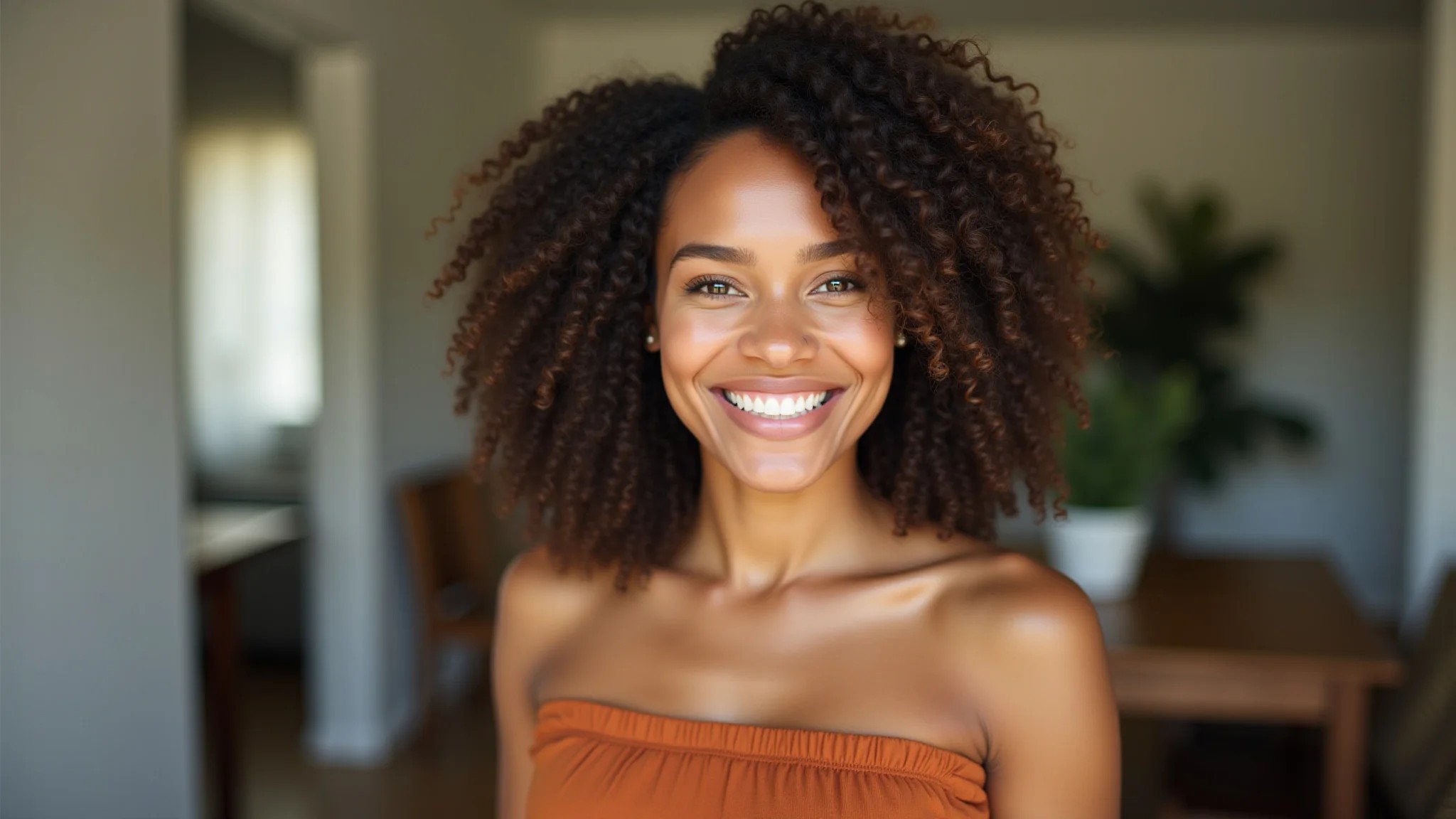 Mulher de pele morena clara sorrindo, vestindo um vestido terracota em um ambiente iluminado.