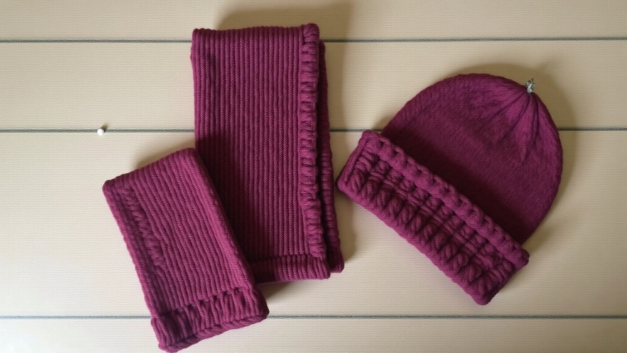 Cachecol e gorro de tricô finalizados, exibidos em fundo rústico de madeira.