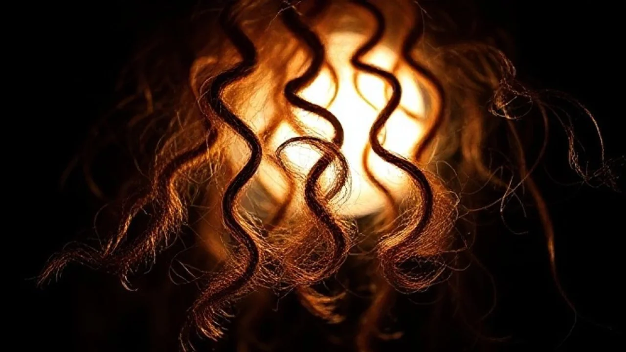 Cabelo crespo com frizz em close-up, mostrando textura irregular e cutículas abertas. Luta contra o frizz.