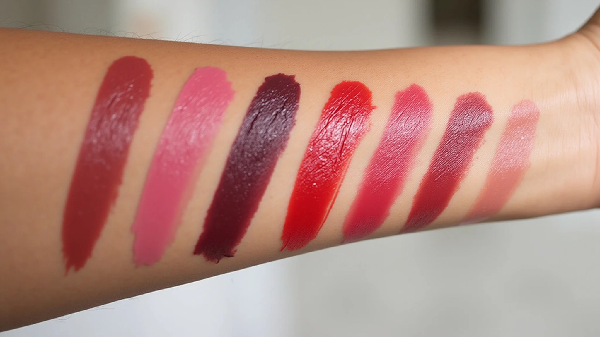 Amostras de batons em tons de vermelho, rosa e vinho em pele morena.