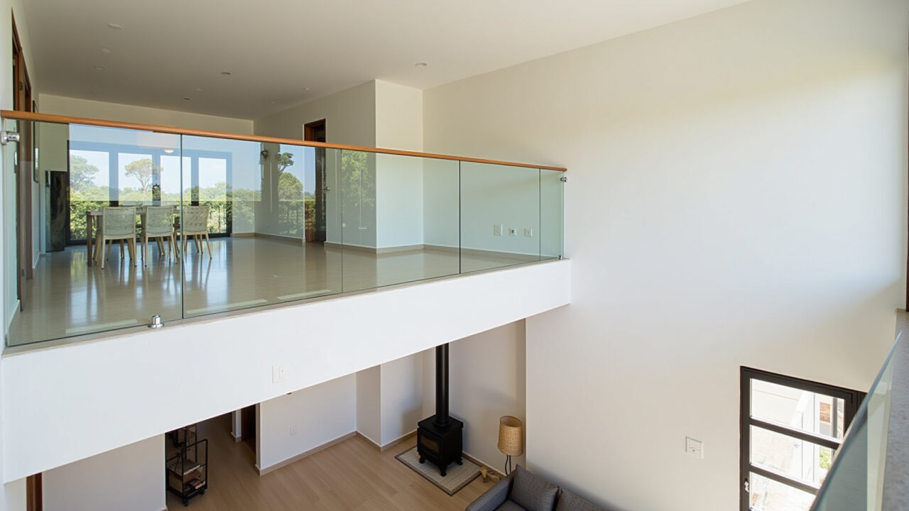 Modern mezzanine with glass railing overlooking a double-height living room, Brazilian design, Mezanino moderno com guarda-corpo de vidro.