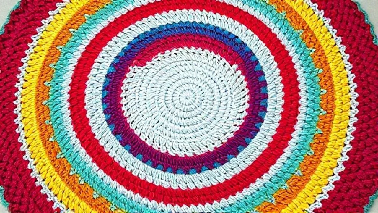 Top-down view of a partially completed round crochet rug with vibrant colors, showing the circular Visão de cima de um tapete de crochê redondo em andamento, mostrando o padrão circular.