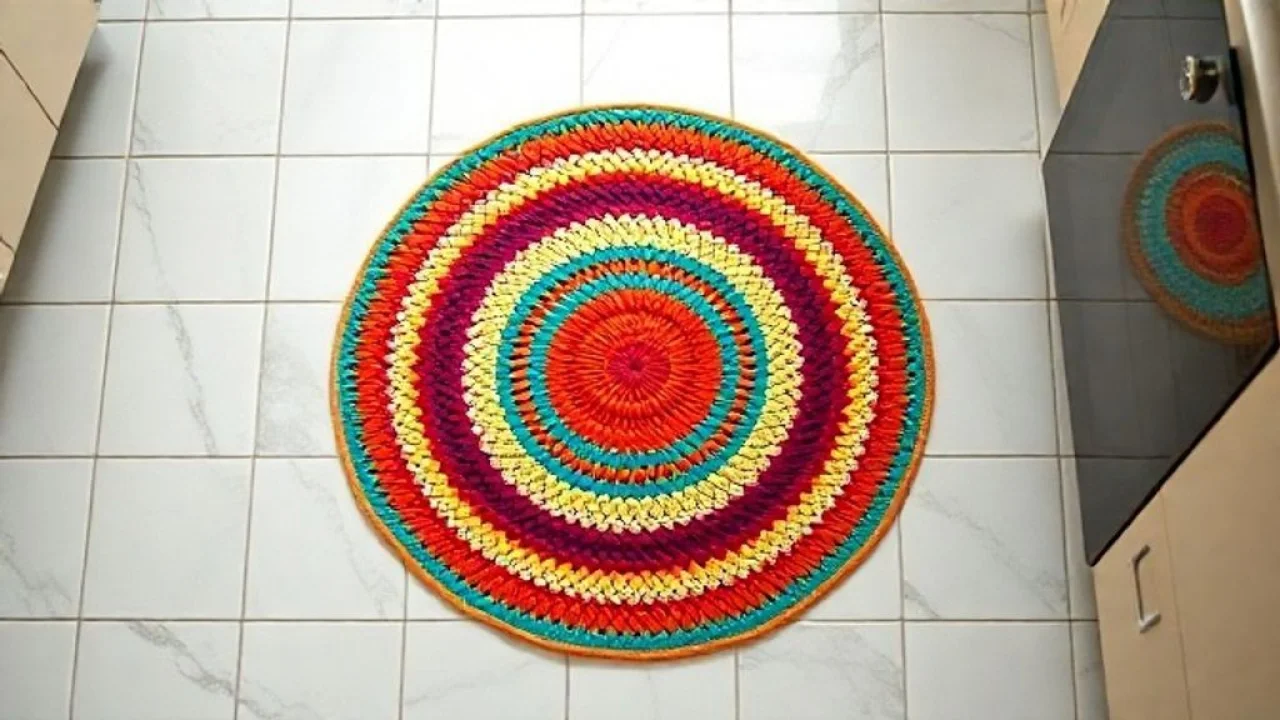 Top-down view of a simple and colorful crochet kitchen rug with a circular pattern on a tiled Tapete de crochê circular simples e colorido em piso de cozinha com azulejos.