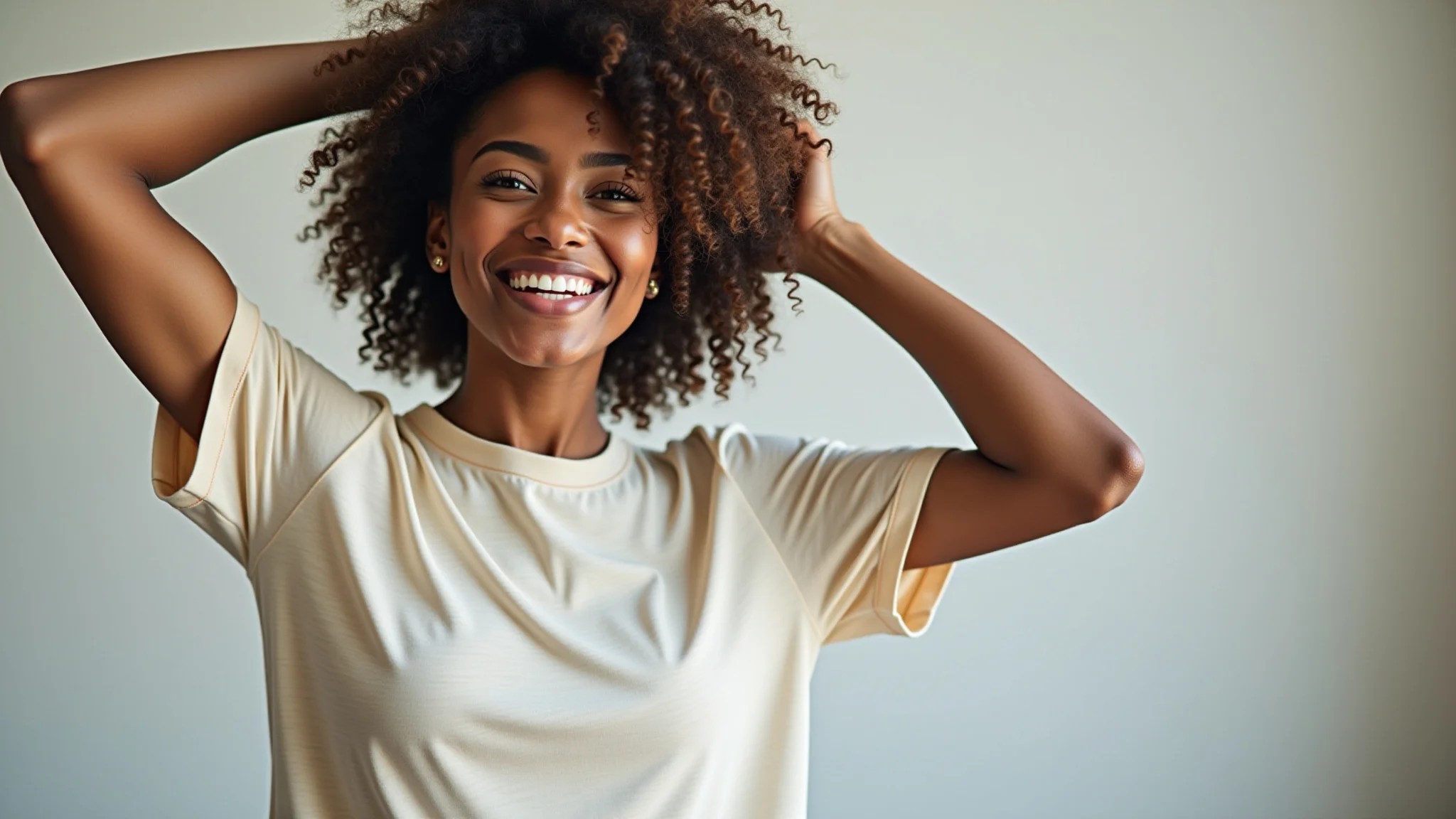 Mulher enrolando o cabelo cacheado em uma camiseta de algodão para plopping, sorrindo.